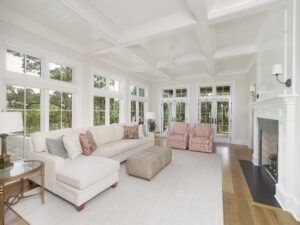 Living room with glass on two walls, fireplace with wood mantel, and painted wood ceiling with coffered beams.