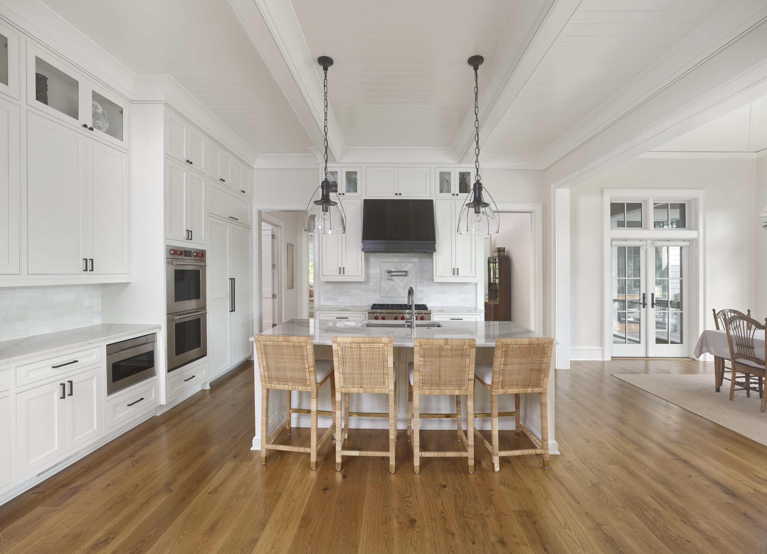 Open white kitchen with large center island and painted wood ceiling with wood beams.