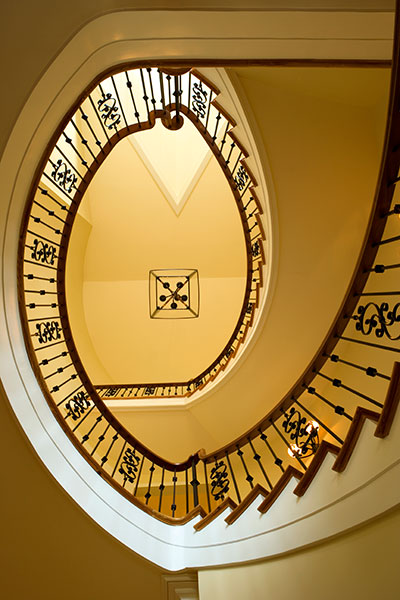 View of curved staircase through center from first floor up to third floor. Decorative iron pickets with stained wood handrail.