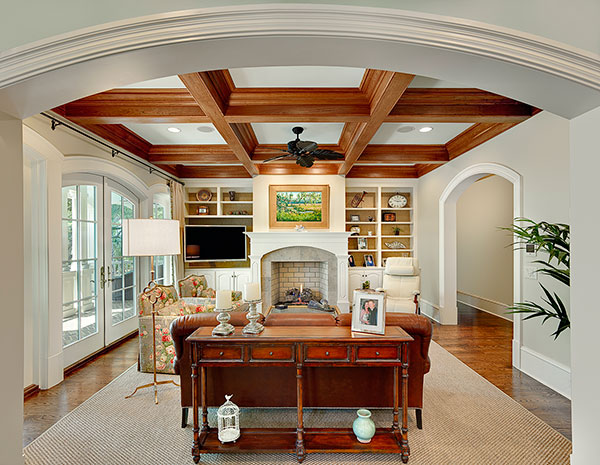 Living room looking through arched cased opening to fireplace with built-ins on either side. Room has stained coffered ceiling and arched French doors that lead to outdoor living.